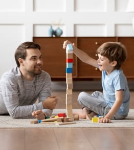 Pai brinca com filho pequeno fazendo torres de cubos.