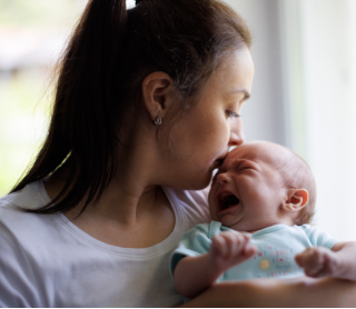 mãe a dar beijinho na testa de bebé a chorar