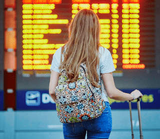 Mulher com mala de viagem na mão a ver um horário de transportes