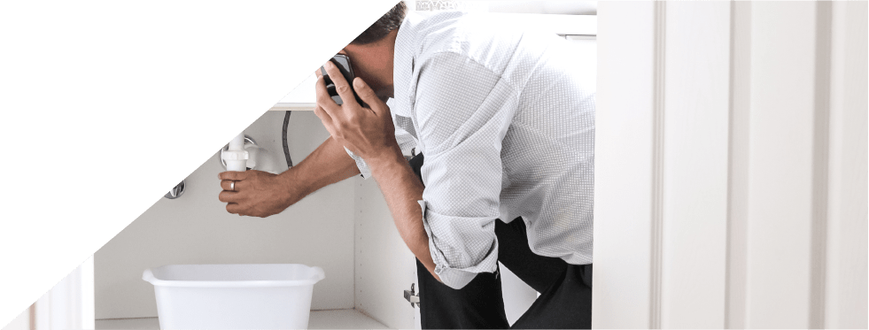 Homem a falar ao telemóvel e a mexer nos canos da casa de banho