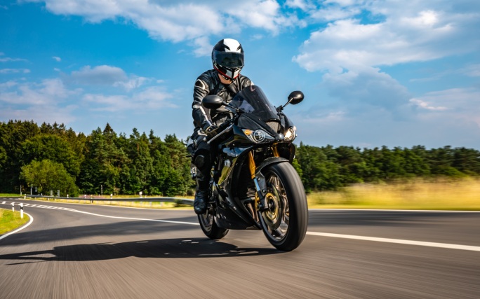 Homem equipado anda de mota na estrada.