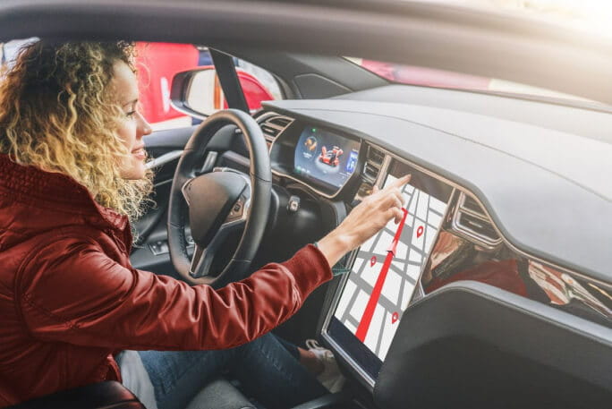 Jovem mulher no interior de um carro elétrico utiliza um painel eletrónico. 