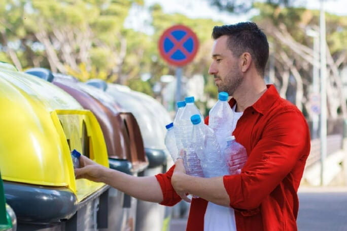 Homem com garrafas de plástico na mão a fazer a separação de lixo no ecoponto