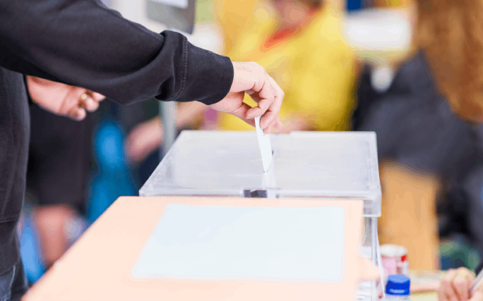 Pessoa não identificada coloca o seu voto dentro de uma urna de voto.