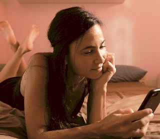Mulher relaxada na cama a consultar o telemóvel num momento de lazer.