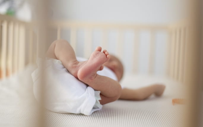 Um bebé dorme deitado numa cama de grades.