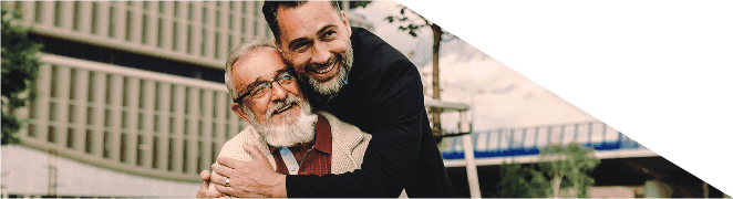 Homem a abraçar carinhosamente um homem mais velho que está sentado num banco de jardim.