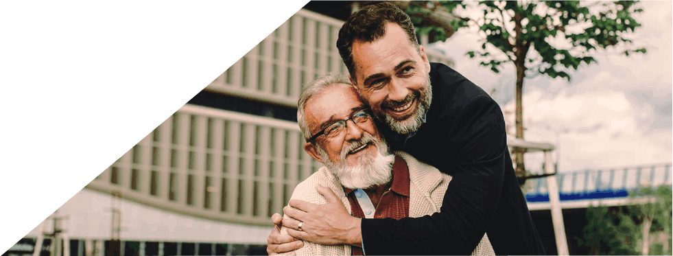 Homem a abraçar carinhosamente um homem mais velho que está sentado num banco de jardim.