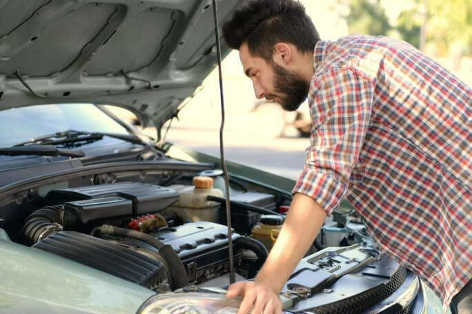 Homem examina o motor de um carro