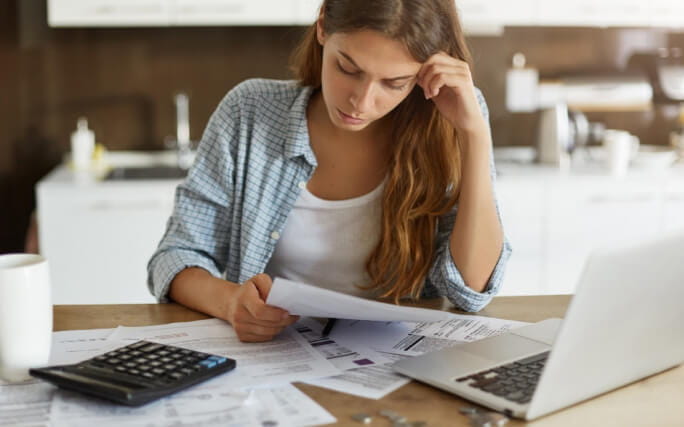 Uma jovem em frente a um computador faz contas para decidir se deve fazer um empréstimo para pagar as dívidas 