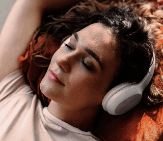 Mulher relaxa de olhos fechados enquanto ouve música com auscultadores.
