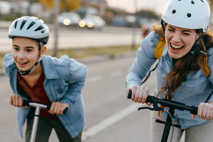 Mãe e filho a passearem, felizes, nas suas trotinetes