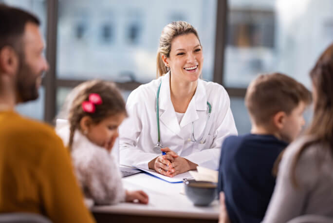 Uma médica sorri para família em consulta de saúde.