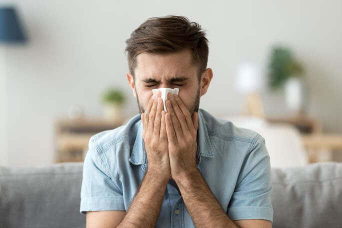 Jovem com alergia ou uma constipação espirra tapando o nariz com um lenço. 