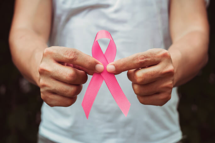 Duas mãos masculinas seguram o laço rosa do cancro da mama.