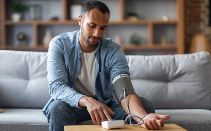 Homem jovem mede a tensão arterial em casa com um medidor de tensão arterial de braço.