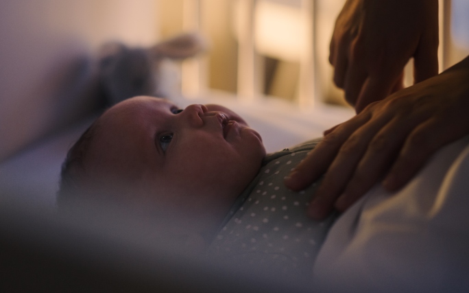Mãos de uma mãe que vigia o sono do bebé, que sofre de insónia infantil.