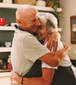 Casal idoso a abraçar-se carinhosamente na cozinha.