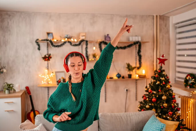 Mulher jovem de headphones dança ao ouvir músicas de Natal.