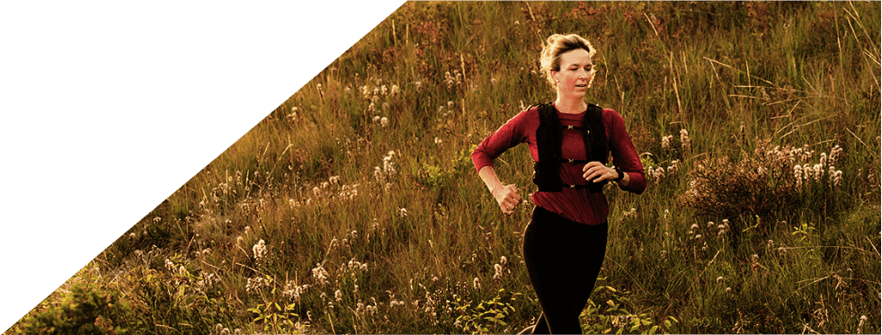 Mulher a correr num trilho ao ar livre ao pôr do sol.