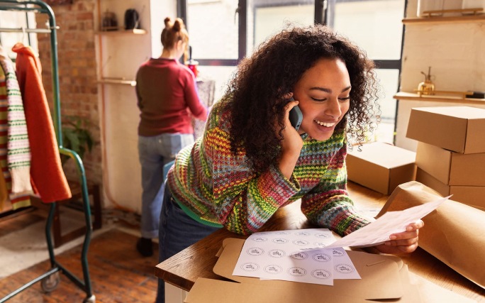 Mulher empreendedora a falar ao telefone enquanto verifica encomendas numa loja de roupa.
