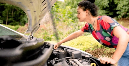 Mulher jovem analisa a bateria do carro.